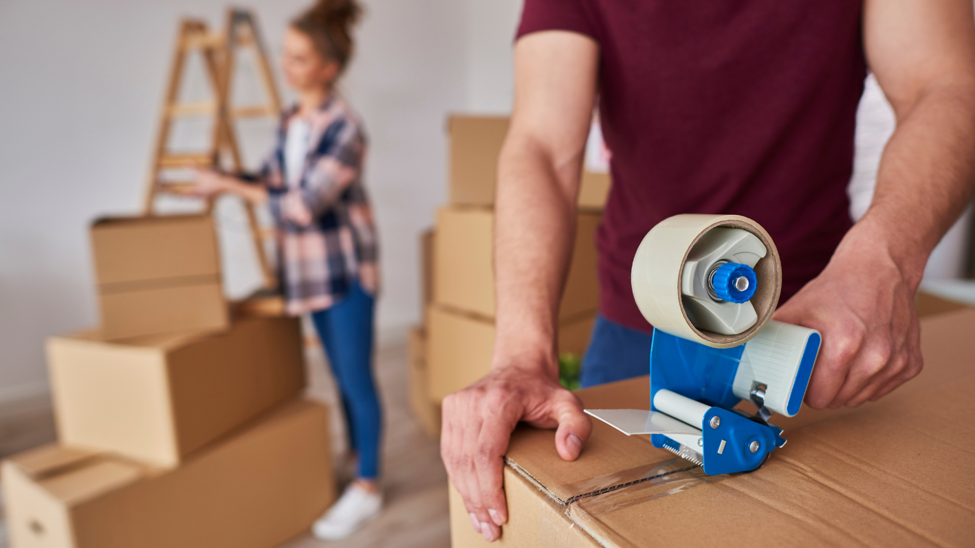 A man and woman moving boxes with a tape dispenser