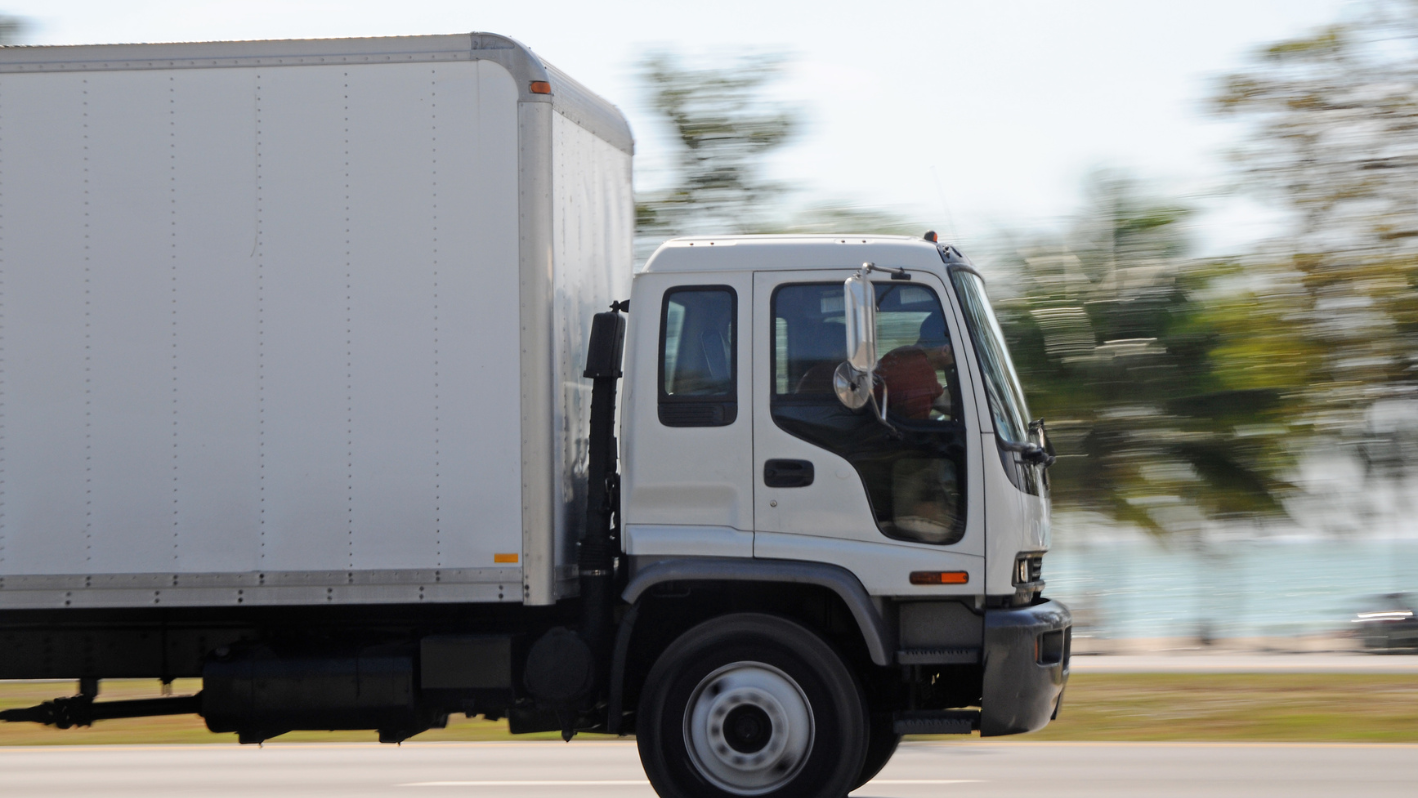 A white truck driving down a street next to a forest