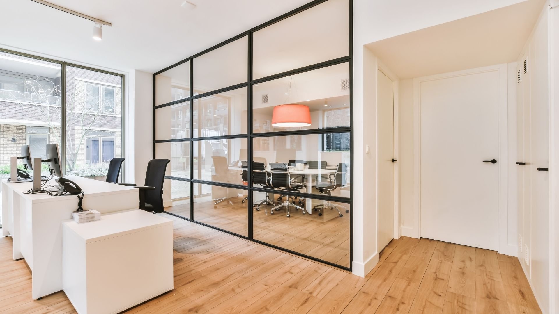 Modern office interior with glass partitions, white desks, and wooden flooring throughout.